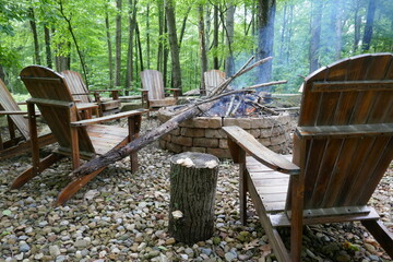 Low angle view of wooden Adirondack chairs around brick fire pit in forest