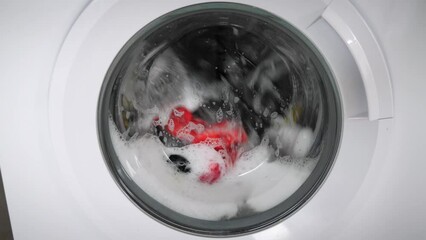 Laundry machine washing clothes with white soap foam. Washing machine with colorful laundry