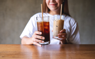 Closeup image of a young woman holding and drinking two glasses of iced coffee