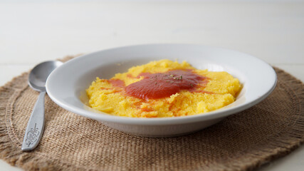 Close view of a plate of hot tasty polenta or cornmeal, served with tomato sauce and spices  