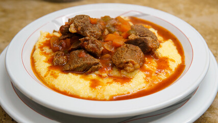  Close view of a plate of hot tasty polenta or cornmeal, served with tomato sauce and some pieces of meat.                         