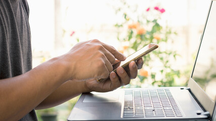 The concept of using the phone is essential in everyday life. Young man using smartphone with computer laptop, During leisure time, work from home. Concept of everyday modern digital technology usage.