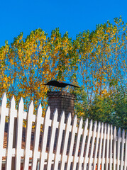 chimenea antigua de ladrillos con árboles de otoño y una cerca blanca