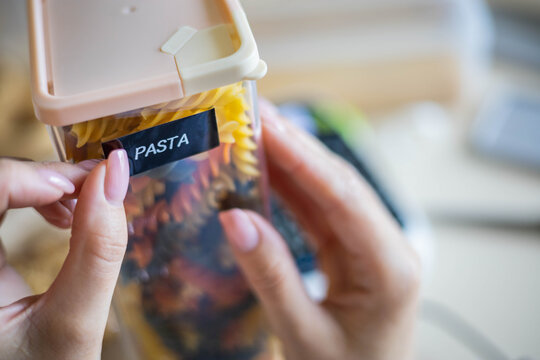 Closeup female hands sticking label on plastic package pasta. Storage organization of food products