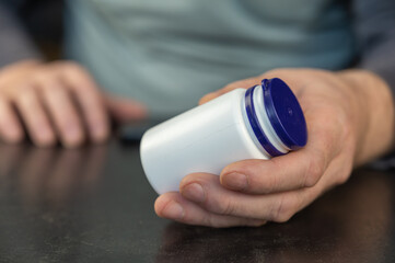 An adult man holds a white vial in his hands.