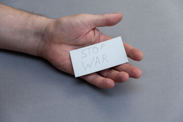 Stop War. Handwritten gray lettering. Open male palm with white business card against gray...
