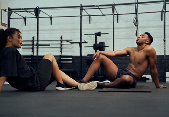 Mixed race friends doing cross fit in the gym. African American male and female resting on the floor after exercising. High quality photo