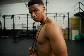 Fototapeta na wymiar African American male holding skipping rope in the gym. Male athlete looking to the camera during exercise. High quality photo