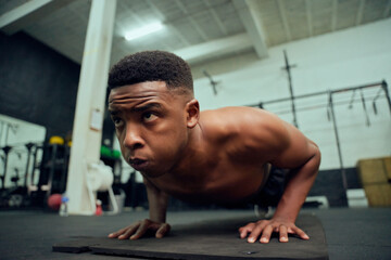 Young African American male doing push-ups in the gym. Mixed race, male personal trainer doing...