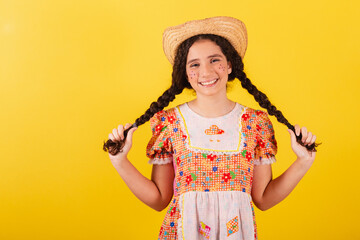 Girl wearing traditional orange clothes for festa junina. Holding hair braids, smiling.