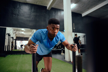 African American male working out intensely during cross fit training. Male athlete pushing the sled in the gym. High quality photo