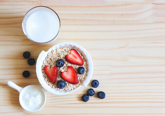 flat lay of  breakfast with oat or granola in white bowl, fresh blueberries, strawberries, a  glass of milk and yogurt on wooden table. Healthy breakfast concept.