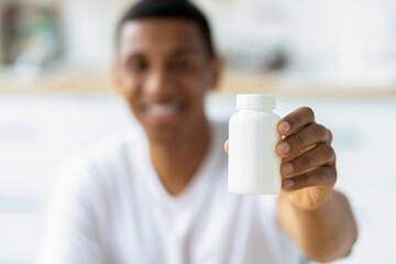 Happy young african american man holding capsules and open bottle. Painkiller, headache medication...
