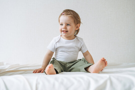 Cuty happy funny baby girl in home clothes sitting on bed at home