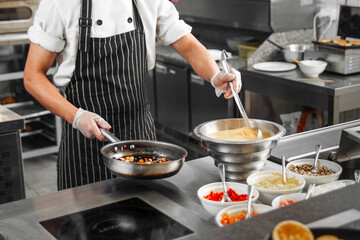 Chef in restaurant kitchen cooking vegetables on a frying pan