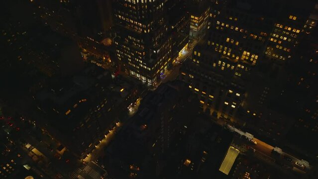 High angle view of streets in night city. Tilt up reveal of high rise buildings with lighted windows in midtown. Manhattan, New York City, USA