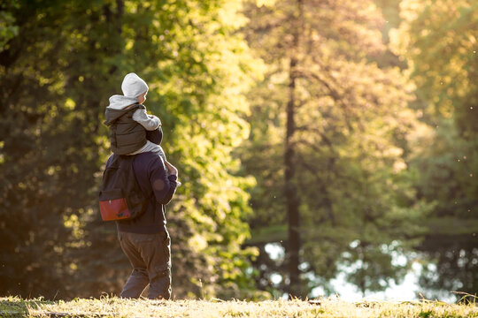 A man and a boy go hiking in the summer forest with a backpack for hiking. Portrait of a father and son sitting on his father's shoulders in the forest at sunset. The concept of travel.