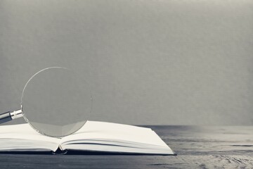 Magnifying glass and opened book on the desk, learning, research searching information concept