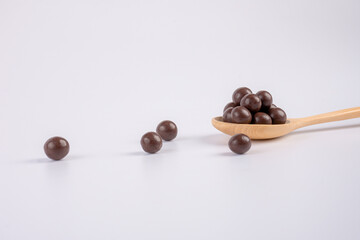 Chocolate balls on wooden spoon on a white background.