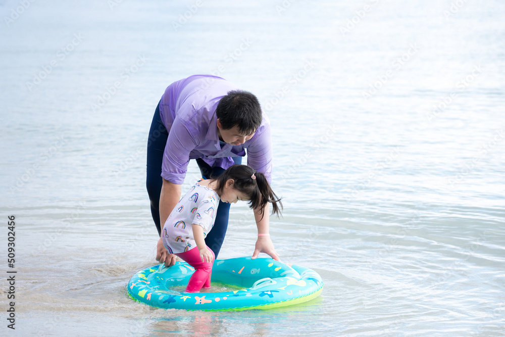 Wall mural Candid image family. Father and daughter playing in sea. Dad is helping to keep little girl on rubber raft to sit in ocean waves on beach. Collect beautiful moments. Summer or spring. Empty space.