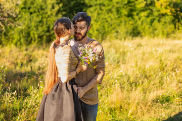 Fototapeta premium young couple hugging in nature, girl holding flowers