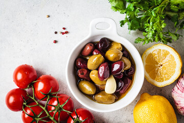 Marinated olives with spice and oil in white bowl, gray background.