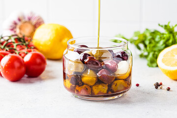 Pickled olives in a jar pour olive oil, white kitchen background.