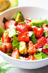 Strawberry, avocado and feta cheese salad with mustard dressing in white bowl. Summer recipe.