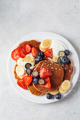 Summer breakfast. Pancakes with strawberries, blueberries, banana and cream on white plate. Vegan recipe.