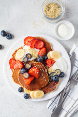 Summer breakfast. Pancakes with strawberries, blueberries, banana and cream on white plate. Vegan recipe.