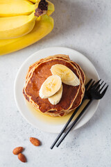 Banana pancakes with syrup on white plate, gray background. Vegan recipe concept.