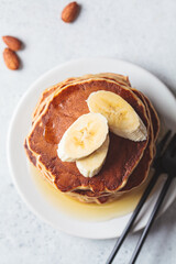 Banana pancakes with syrup on white plate, gray background. Vegan recipe concept.