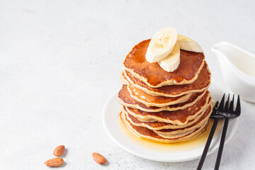 Banana pancakes with syrup on white plate, gray background. Vegan recipe concept.