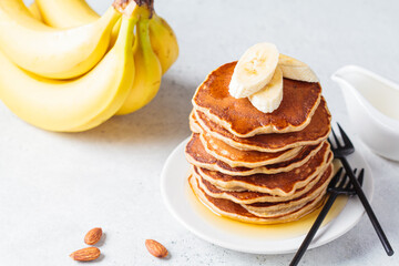 Banana pancakes with syrup on white plate, gray background. Vegan recipe concept.