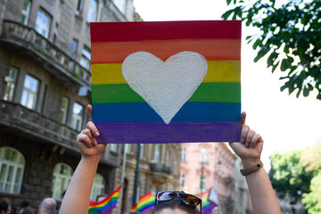 Woman holding rainbow flag heart placard sign, symbol of LGBT love during Pride Parade. Equality...