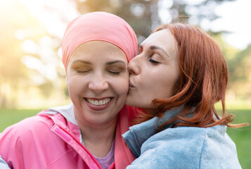 couple of mature lesbian women, kiss on the face, cancer survivor woman with a pink scarf. fighters