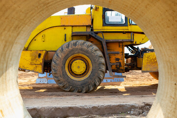 Fototapeta na wymiar Heavy loader at the construction site. View of the wheel loader through the concrete pipe. Construction equipment for earthworks.