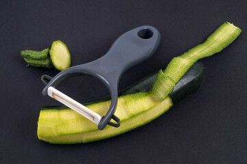 Courgette en partie épluchée avec un épluche légume sur fond noir