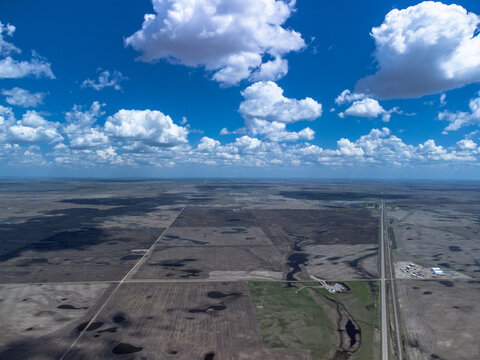 Aerial view of long, straight prairie highways stretching under a cloudy blue sky