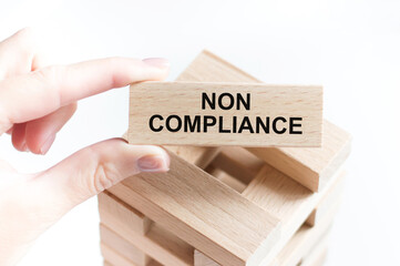 NON COMPLIANCE inscription on a wooden bar in the hands of a person, business concept