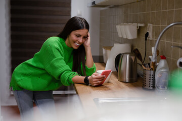 Beautiful woman drinking coffee and using the phone in the kitchen