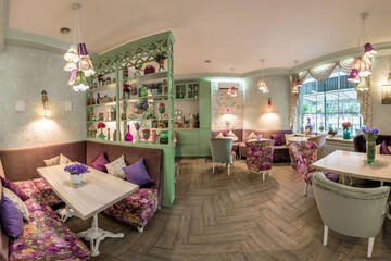 Cozy cafe interior with soft sofas and chairs, shelves with romantic trinkets, lampshades, window...