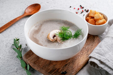 Cream soup with champignons and dill in a white bowl on the table with croutons