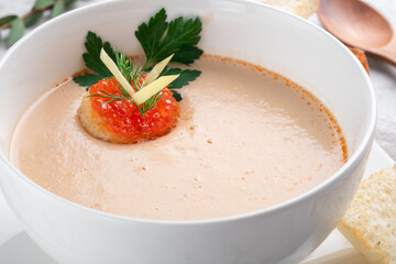 Fish cream soup with salmon in a white bowl decorated with crackers with red caviar, close up