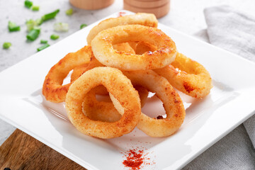 Deep-fried onion rings on a white plate with seasonings, close up