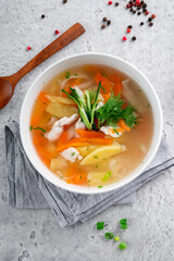 Chicken soup with vegetables and herbs in a white bowl served on the kitchen table, top view