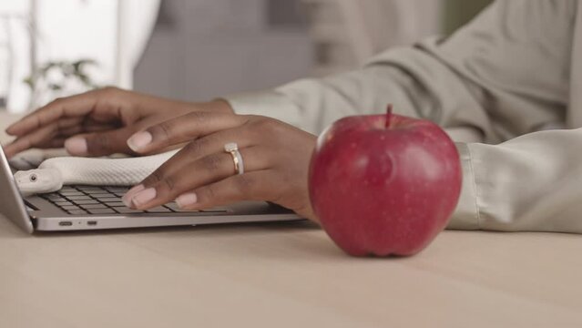 Slowmo closeup of white pet snake crawling on laptop keyboard and office desk, wrapping itself around red apple while unrecognizable Black woman typing on laptop working from home