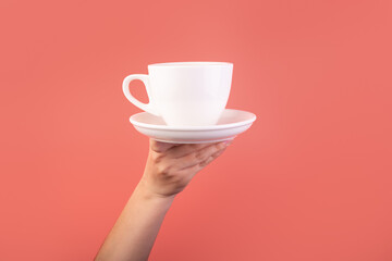 Breakfast and coffee theme: woman's hand holding white empty ceramic coffee cup isolated on a pink background, advertising coffee