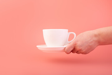 Breakfast and coffee theme: woman's hand holding white empty ceramic coffee cup isolated on a pink background, advertising coffee