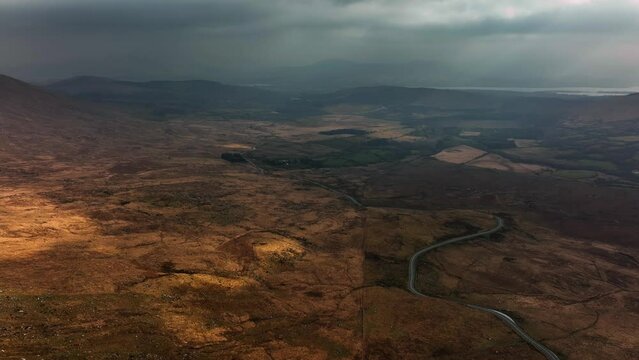 Killarney, Kerry, Ireland, March 2022. Drone pulls northwest while descending towards Molls Gap under a moody sky with views south towards Carhoomeengar with Kenmare in the distance.
